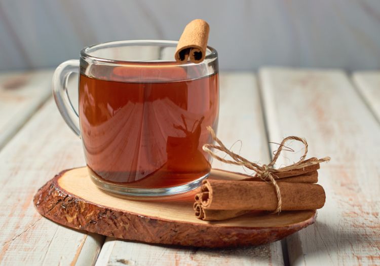 Uma xícara de chá de canela, com canela em paus ao lado - chá indicado para diabéticos.