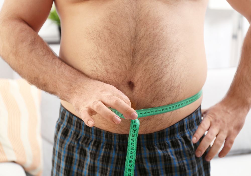 Um homem medindo a barriga inchada com uma fita métrica Suco para desinchar.