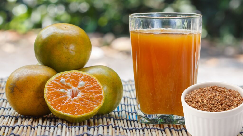 Laranjas em cima de uma mesa; um pote com linhaça moída e um copo com suco de laranja e linhaça batidos.