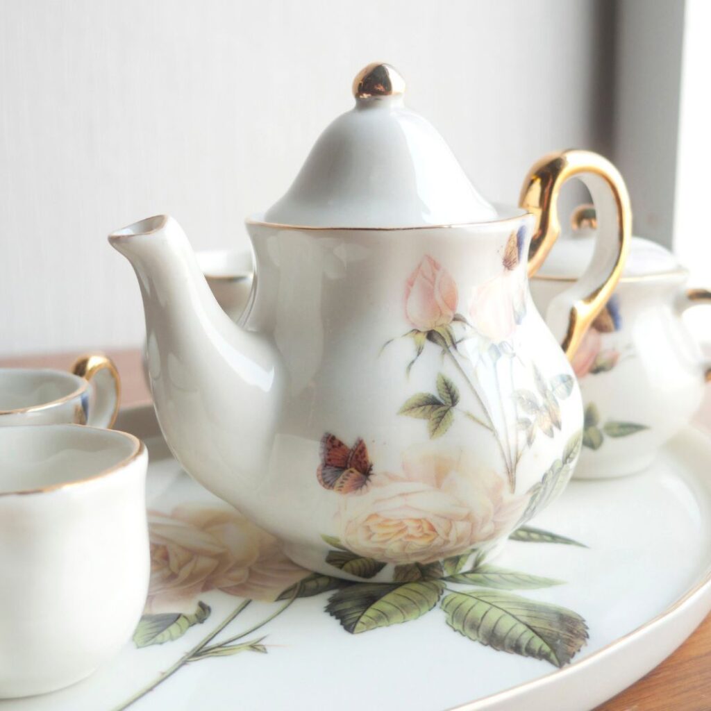 Um bule de porcelana com duas xícaras de porcelana ao lado, ambos em cima de uma bandeja de porcelana.