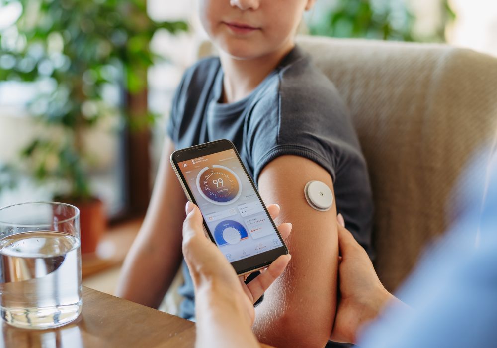 Uma pessoa com adesivo de medir glicemia para diabetes e outra pessoa com aparelho na mão para ver o resultado.