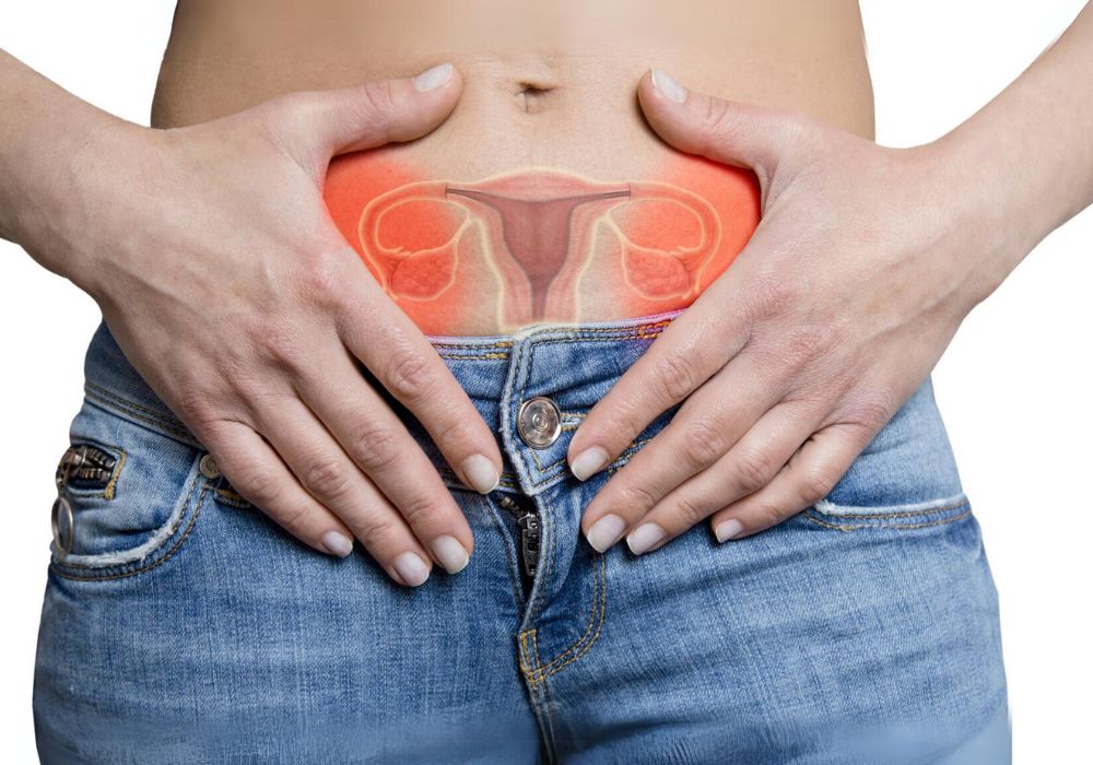Uma mulher de calça diz, com as mão na altura do útero e o desenho de um útero, no tom vermelho indicando dor.