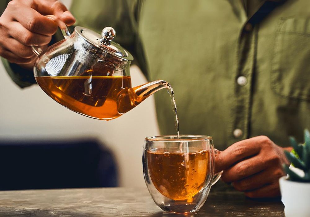 Um homem servindo uma xícara de chá mate com um bule de vidro.