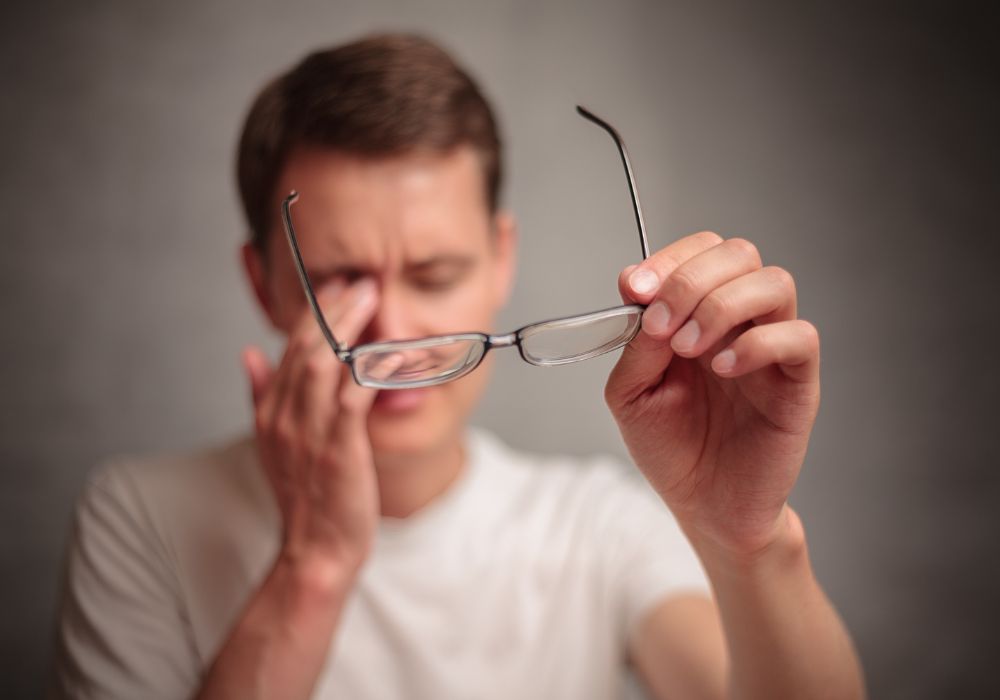 Um homem com uma das mãos nos olhos e a outra segurando os óculos.