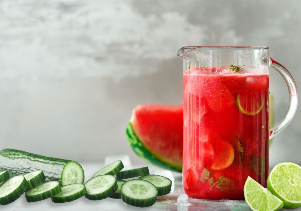 Um copo com suco de melancia, limão e pepino; e os ingredientes aos redor.